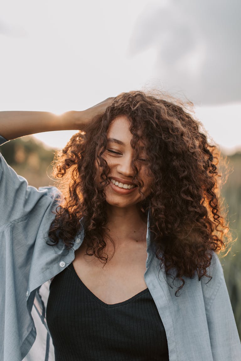 A cheerful woman with curly hair enjoys a carefree moment under the sun in an outdoor setting.